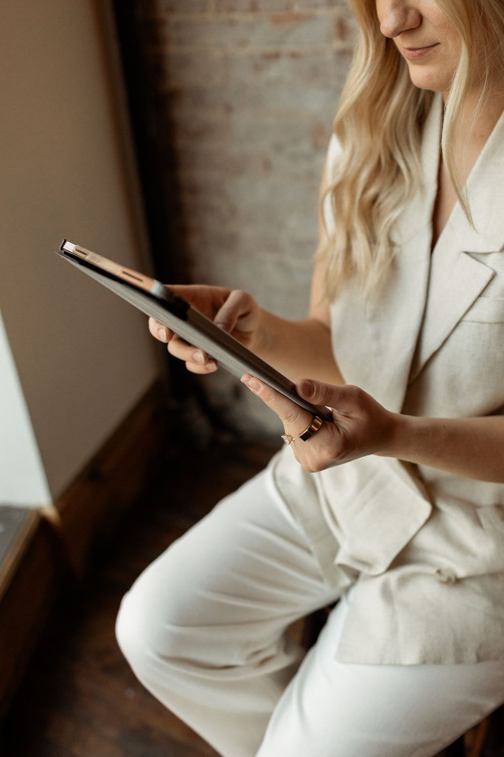 Woman in white blazer sitting casually while using smartphone device in natural lighting.