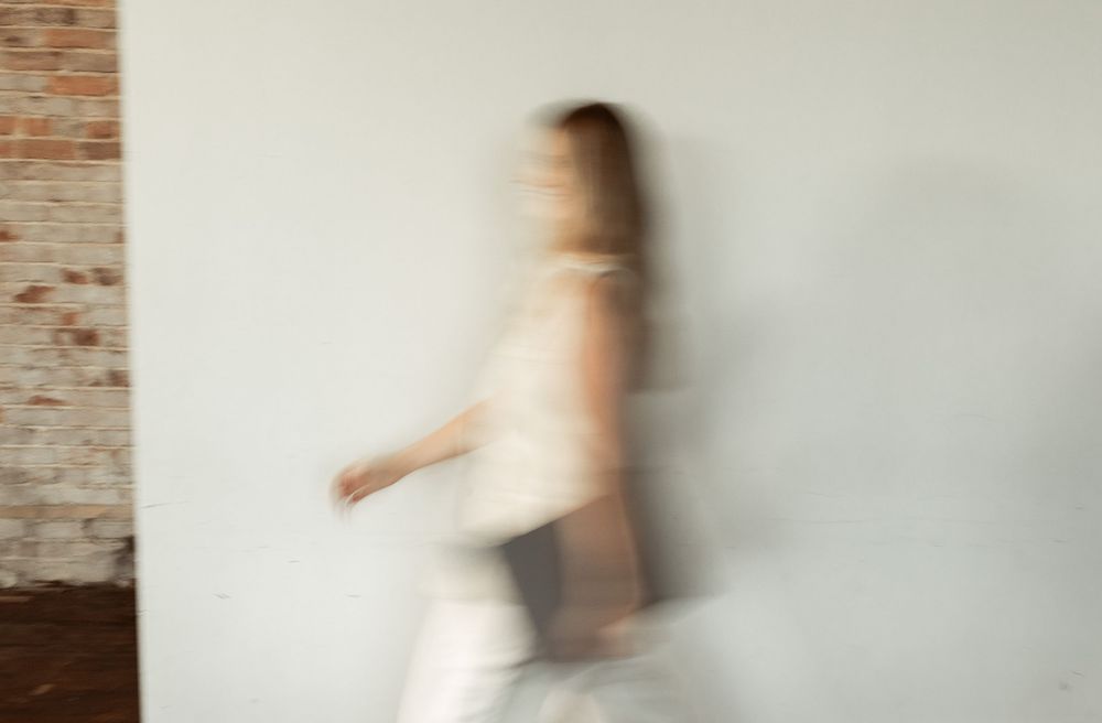 Blurred motion photograph of a figure in white dress walking past a brick wall.
