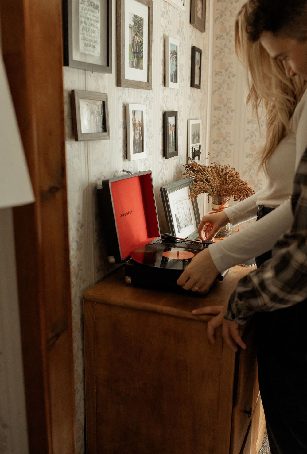 Person in vintage dress examines old photographs on a stone wall in a rustic interior setting.