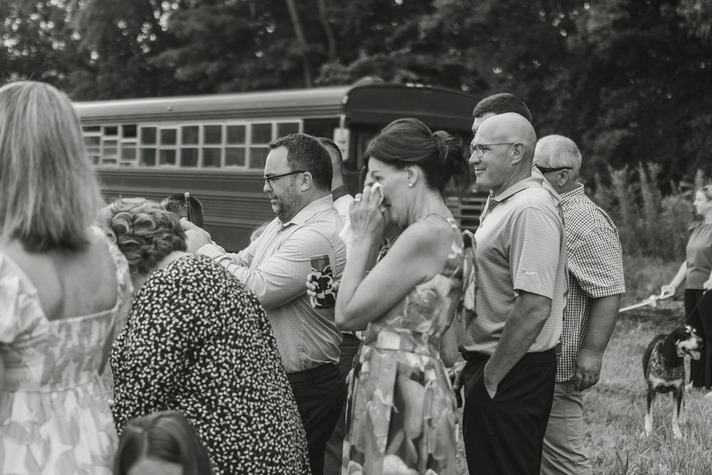 A crowd of people stand outdoors near a yellow school bus in this vintage black and white photograph.