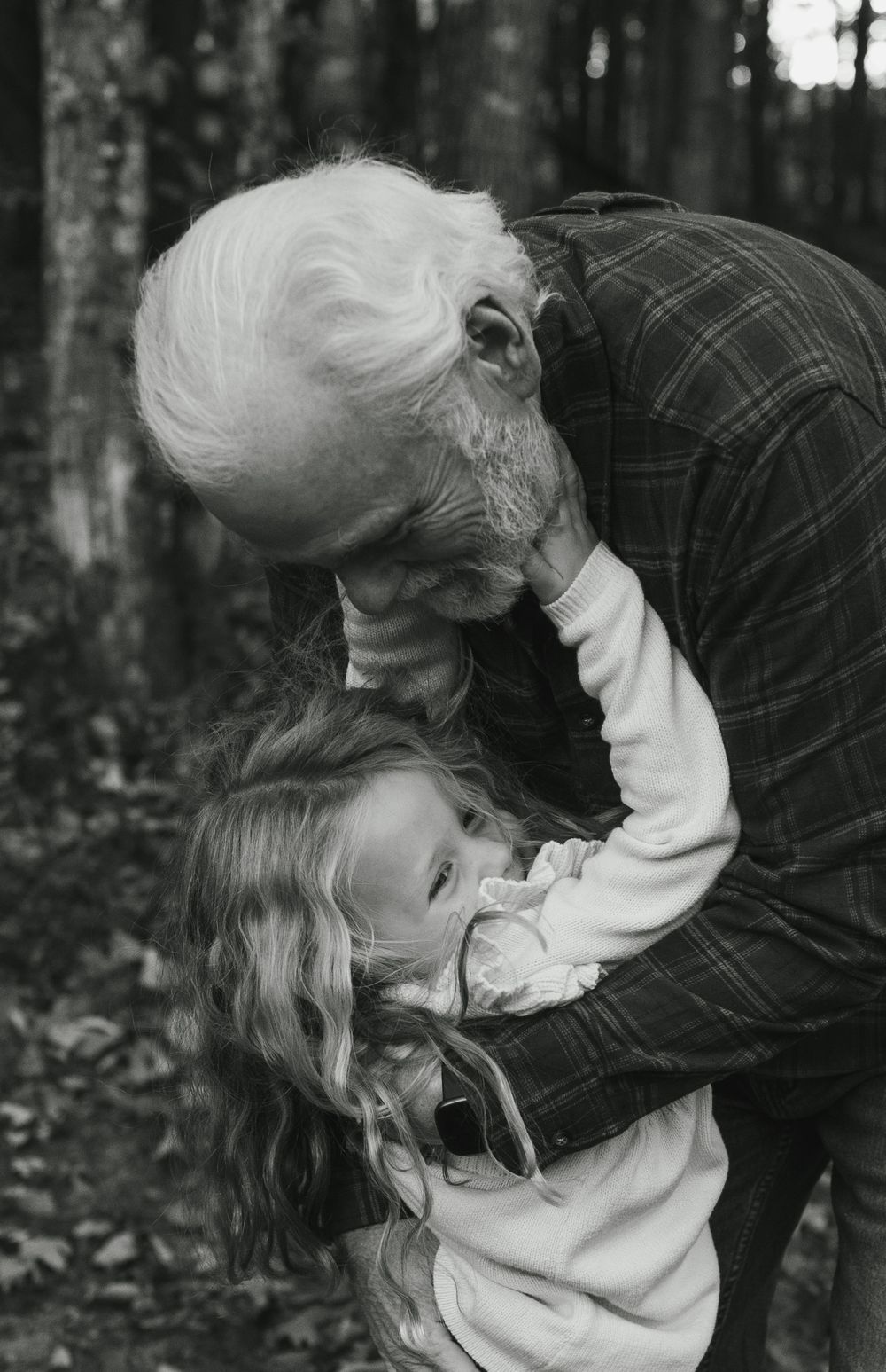A tender moment captured in black and white as an elderly person in plaid bends down to embrace a young child outdoors.