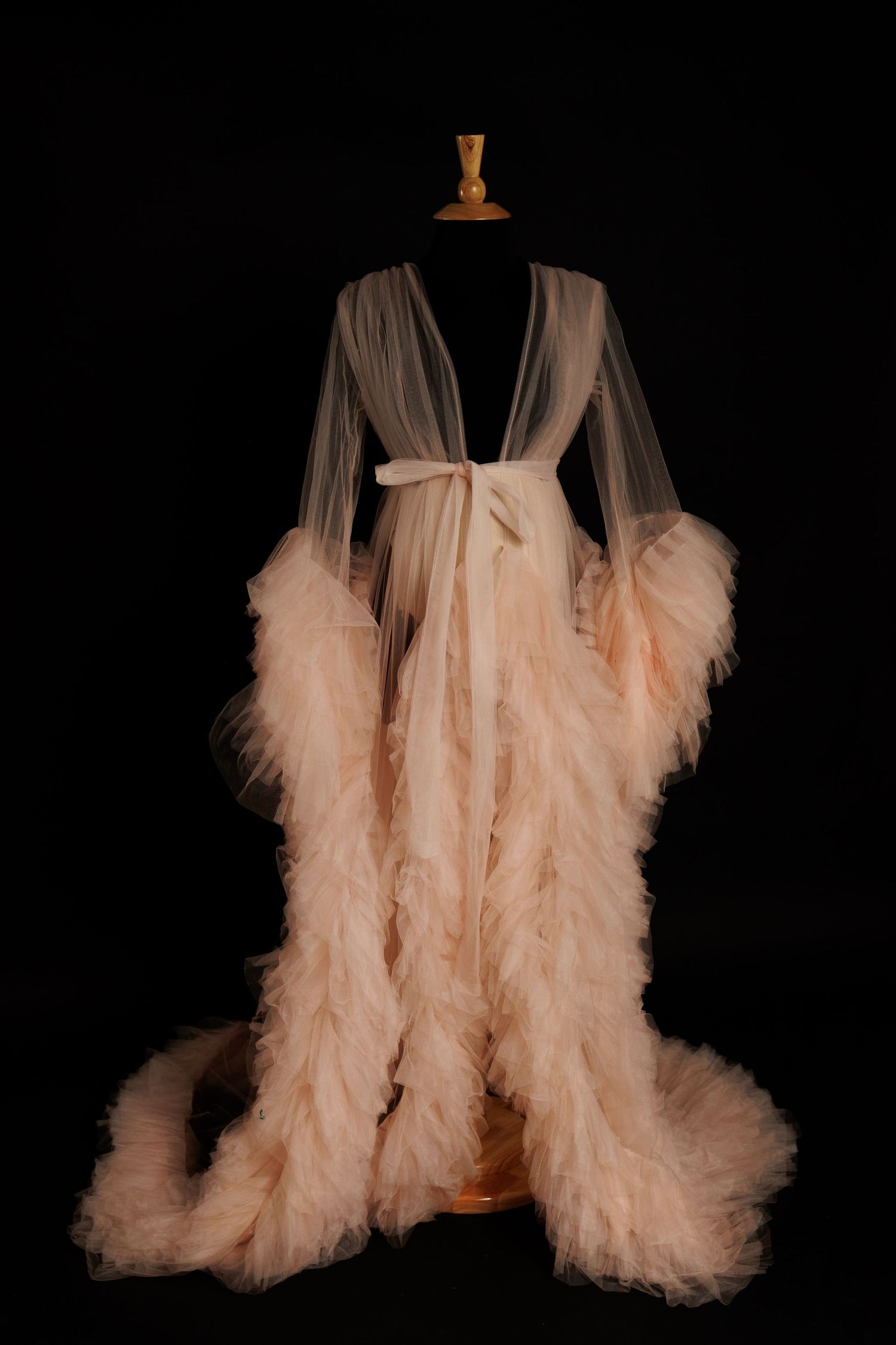 A delicate peach-colored tulle robe with flowing layers and ruffles displayed against a black background.
