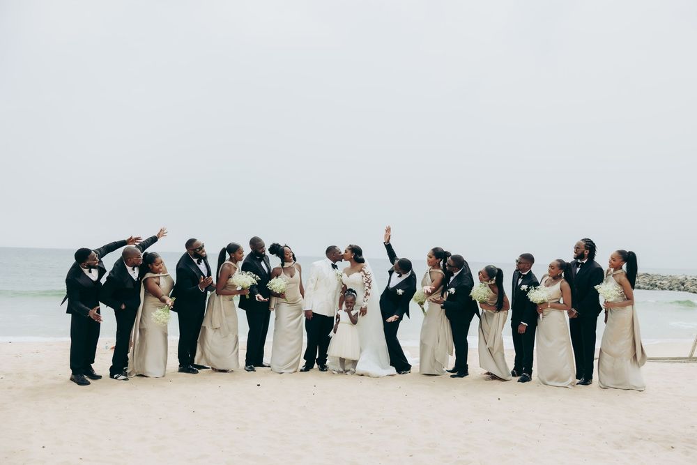 Wedding party lined up on beach creating silhouettes against light background.