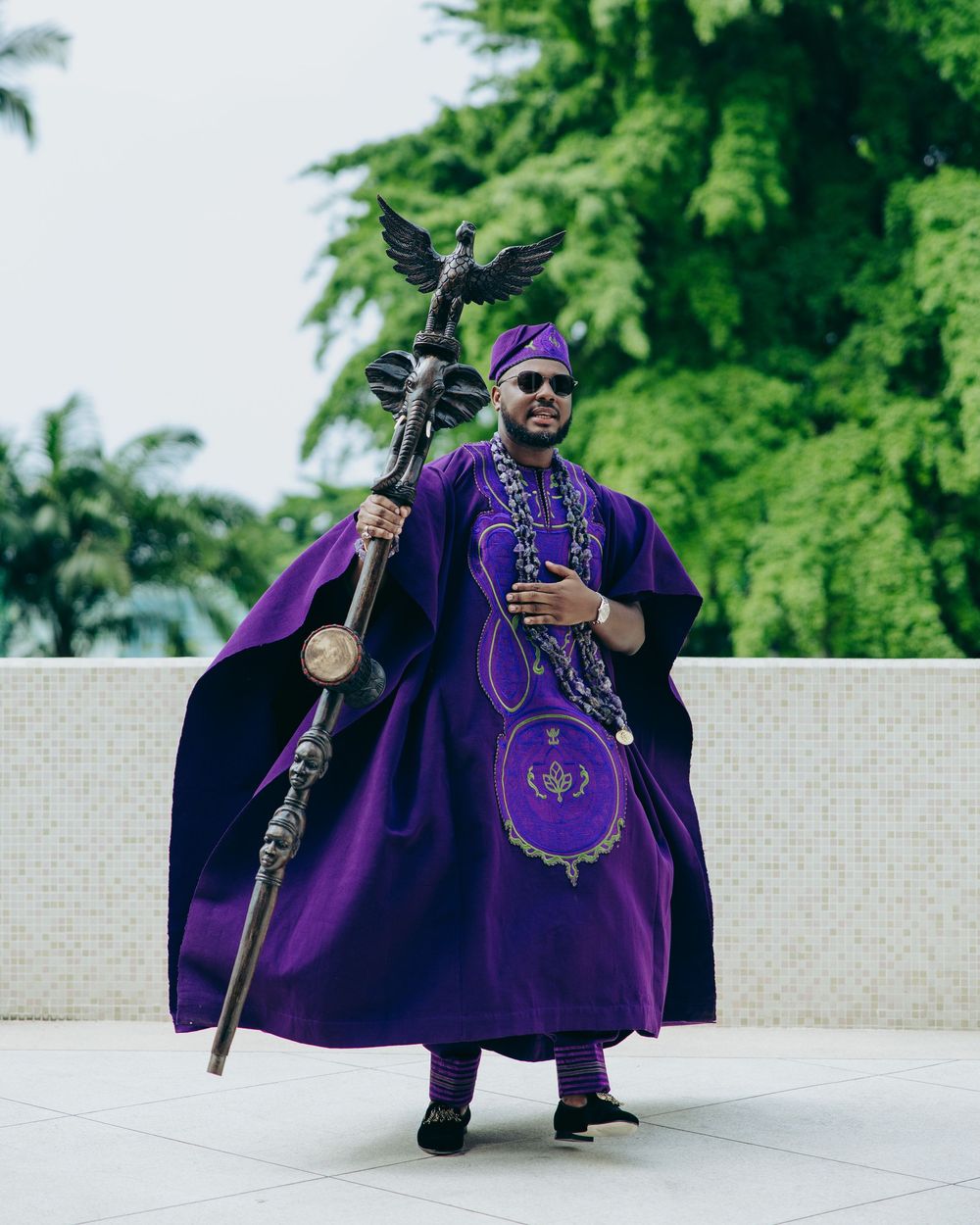 Figure in royal purple ceremonial robe posing dramatically outdoors.