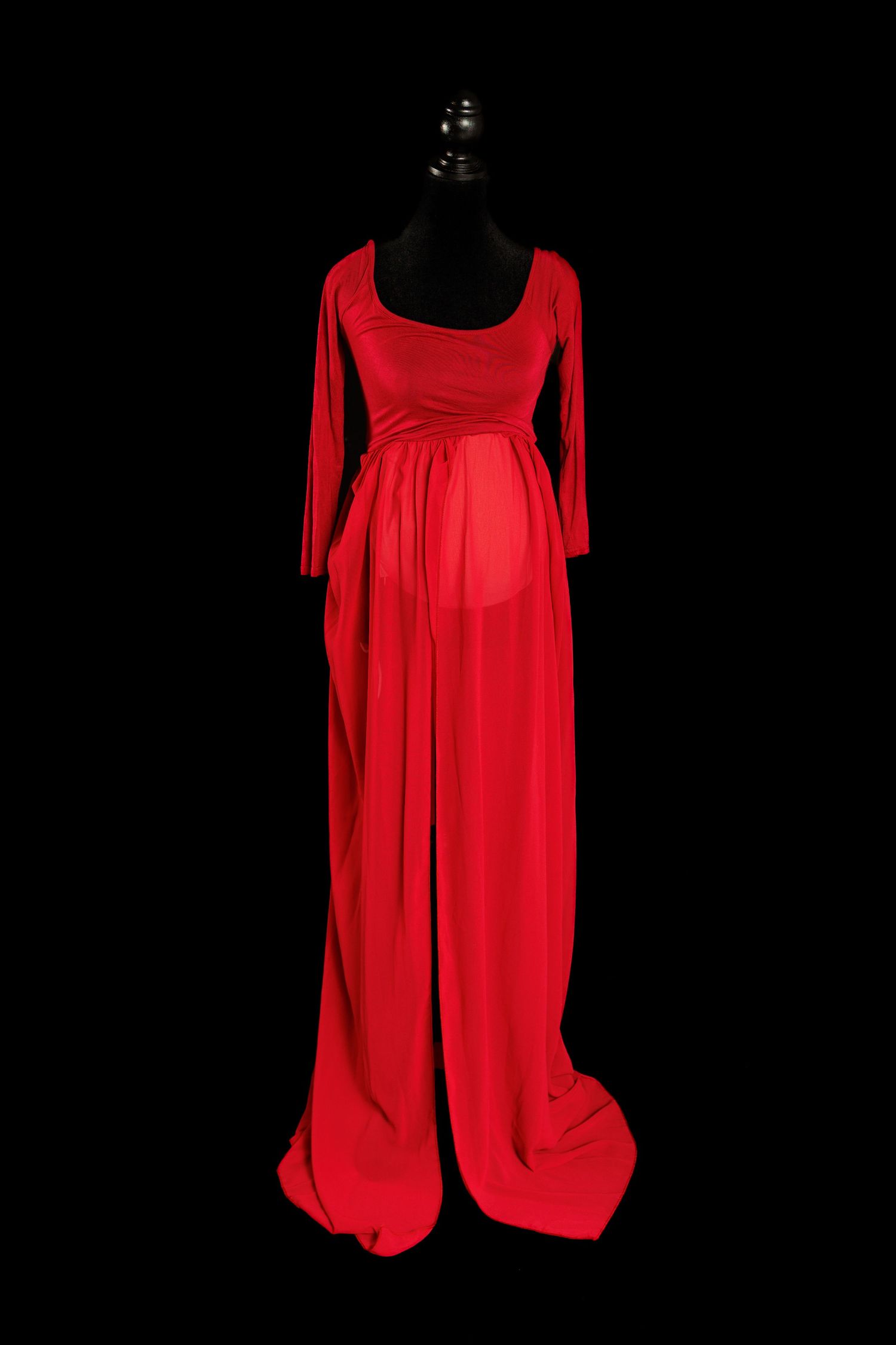 A long red formal maternity dress with three-quarter sleeves and empire waist displayed on a black mannequin against dark background.