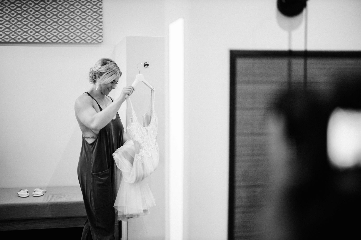 A black and white image showing preparations with a white dress hanging in a dressing room.