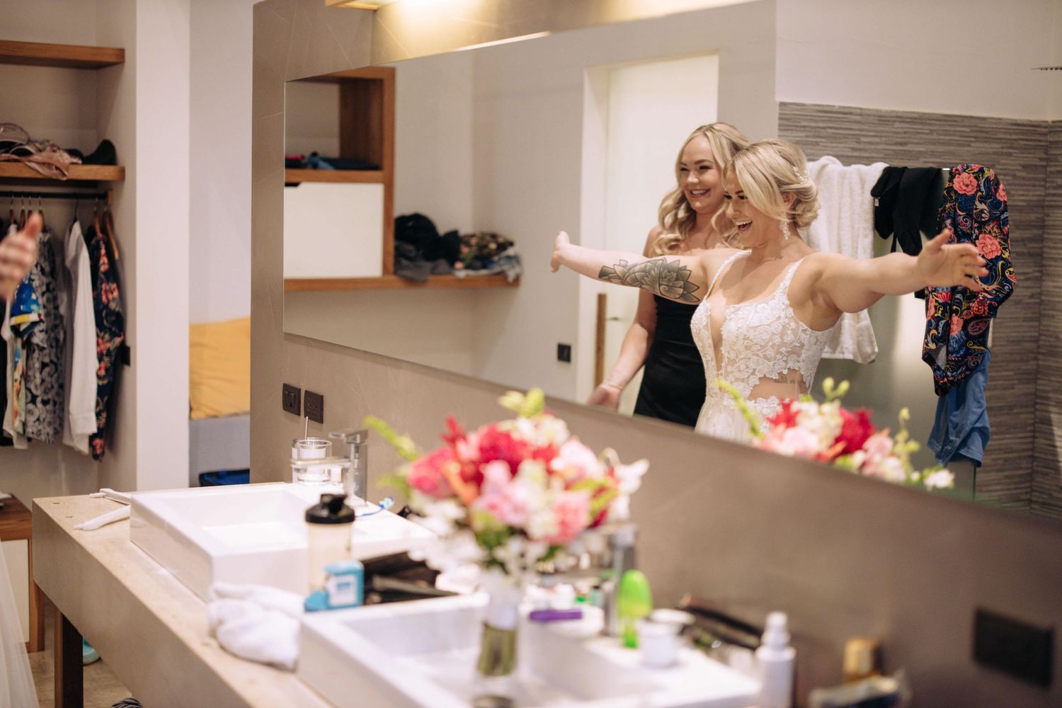 A dressing room scene with a vanity mirror, flowers, and someone getting ready in an elegant white dress.
