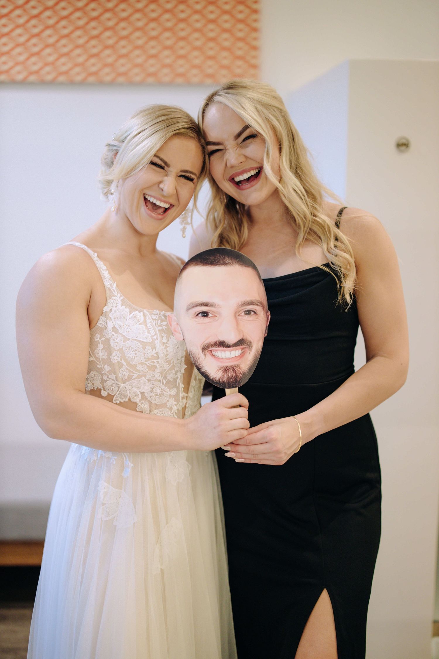 Two people share a joyful moment together in formal attire at what appears to be a wedding preparation setting.