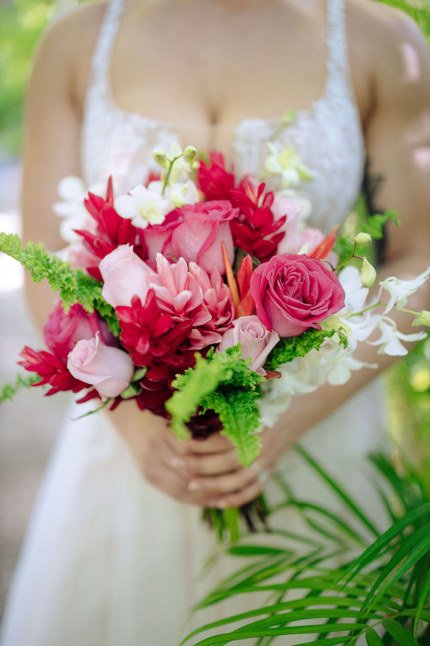 A pink and red rose bouquet with white accents and green foliage held against a light background.