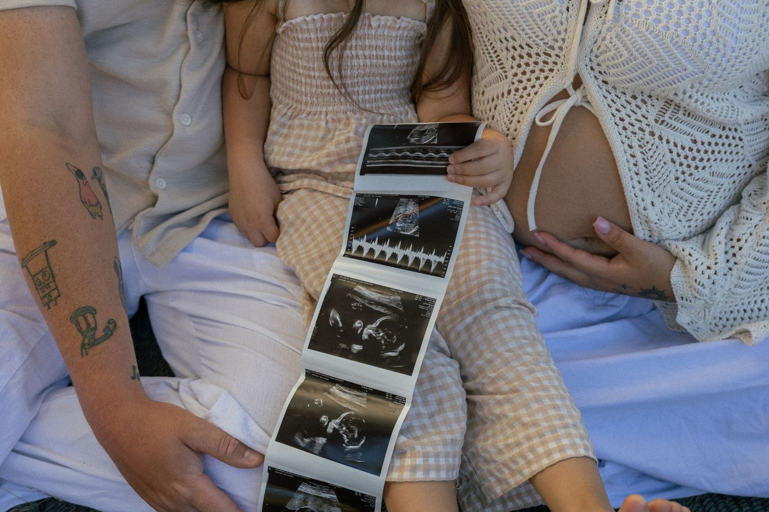 A family celebrating their pregnancy. The family is wearing lace, gingham, earth tones in their maternity photos while holding an ultrasound
