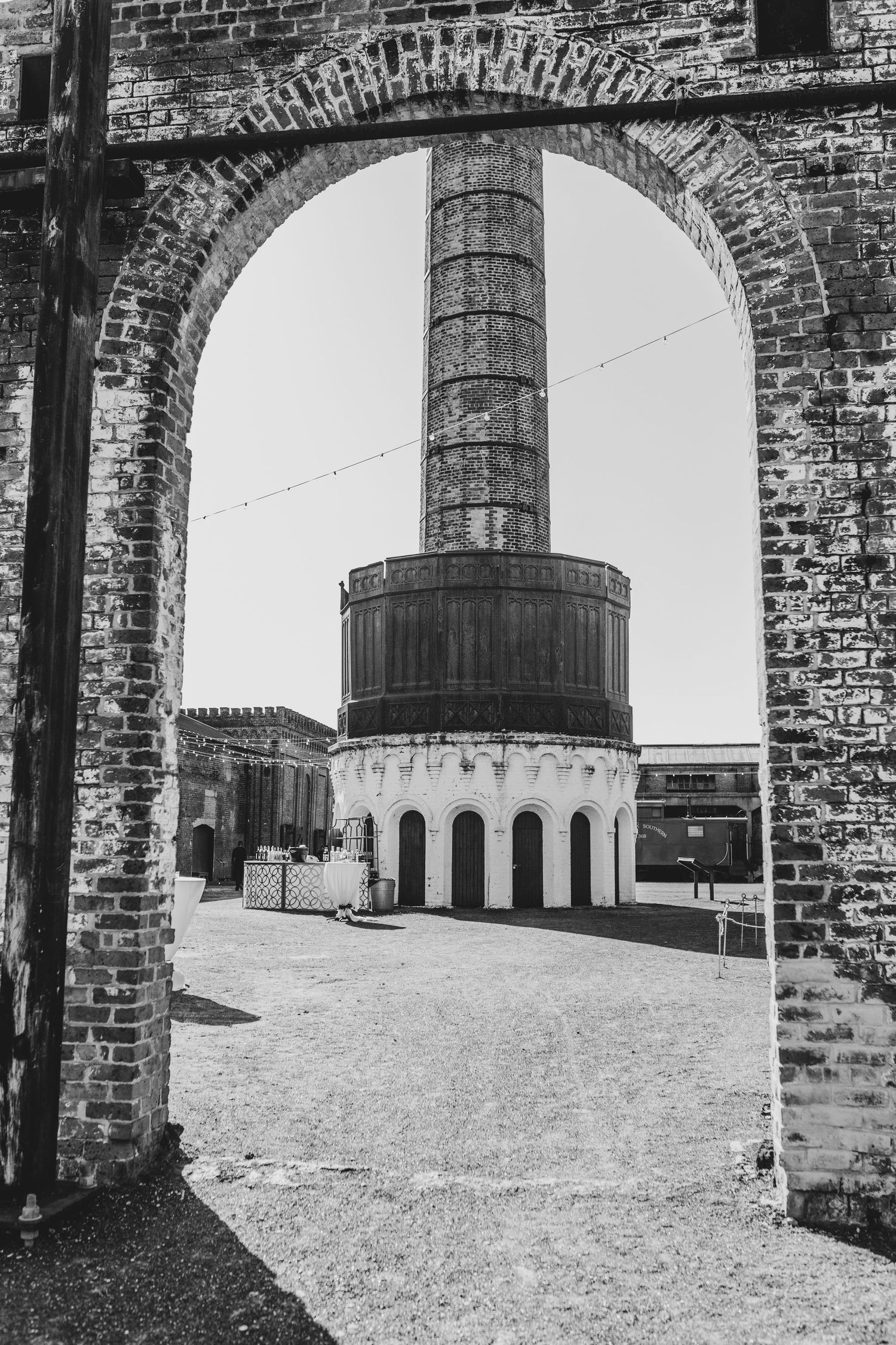 Historic brick archway frames view of old industrial chimney and circular building at abandoned factory site.