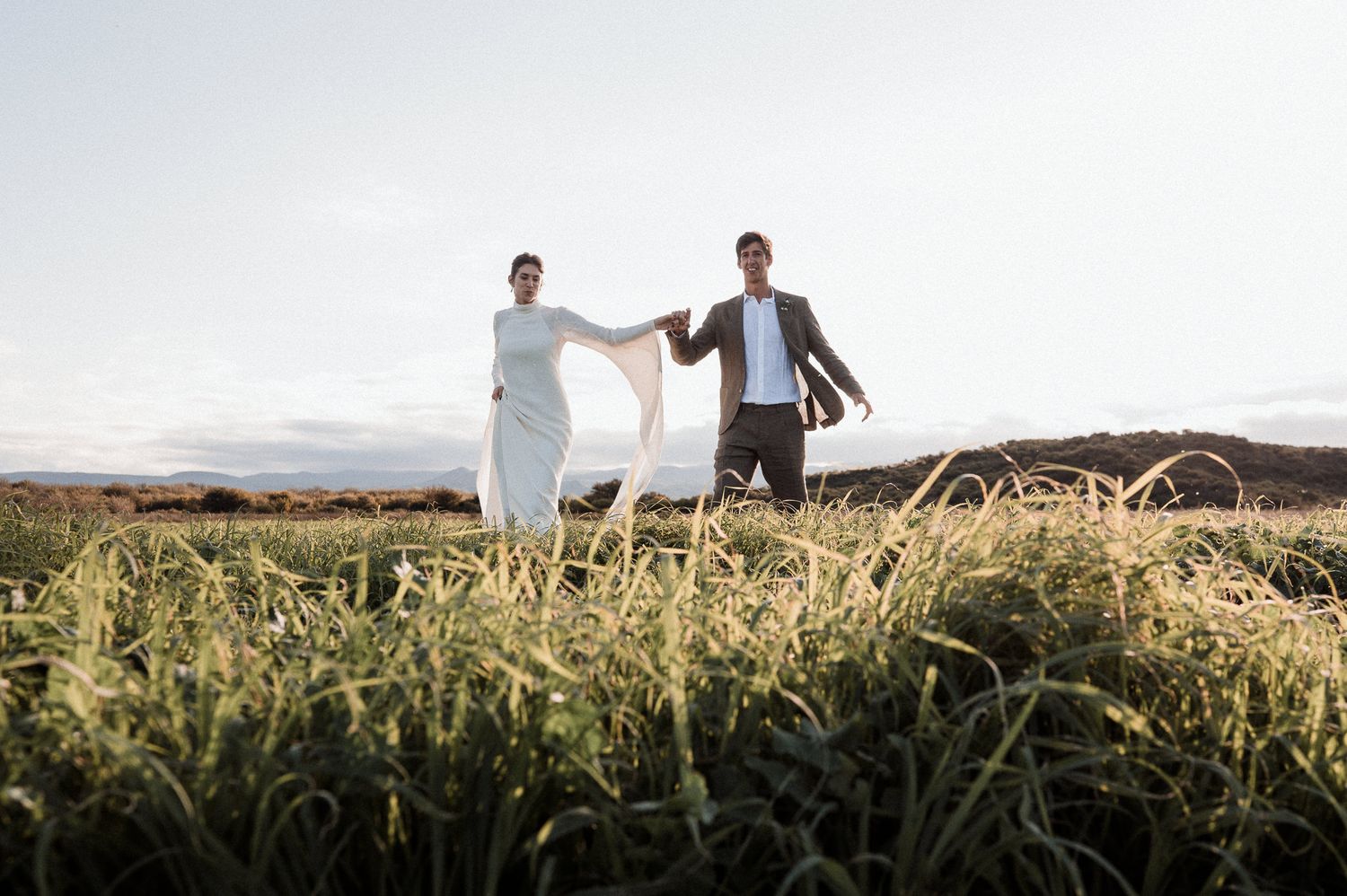 Intimate wedding portrait of newlyweds embracing on manicured lawn during golden hour.