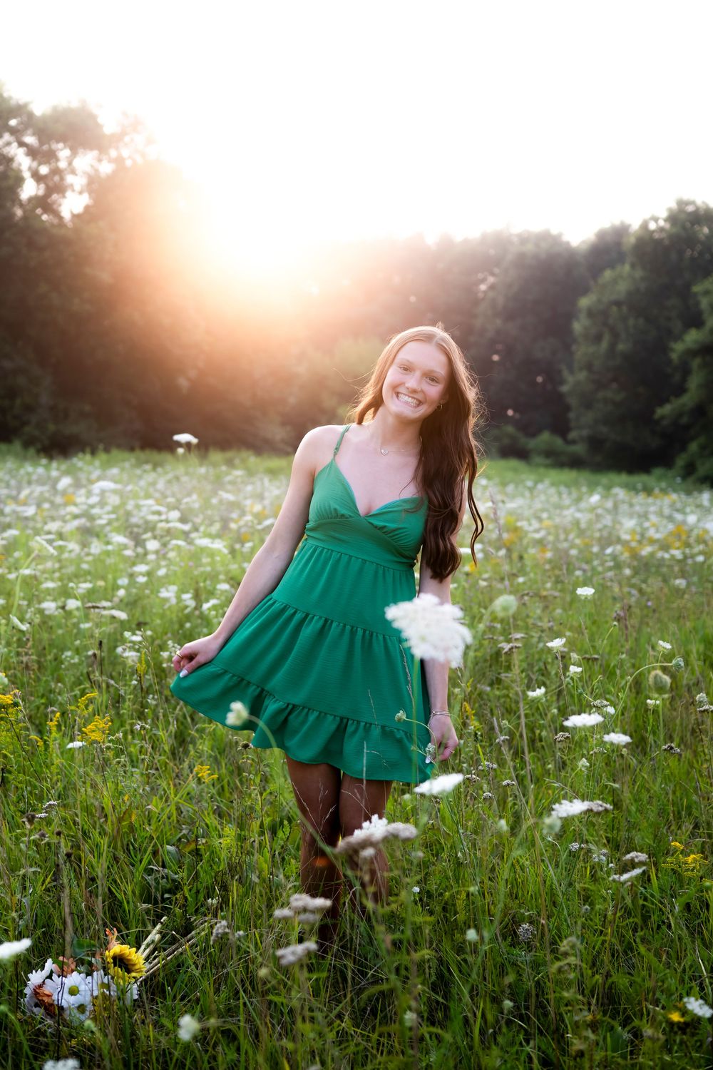 Emerald green dress flows in a meadow of white daisies during golden hour sunset.