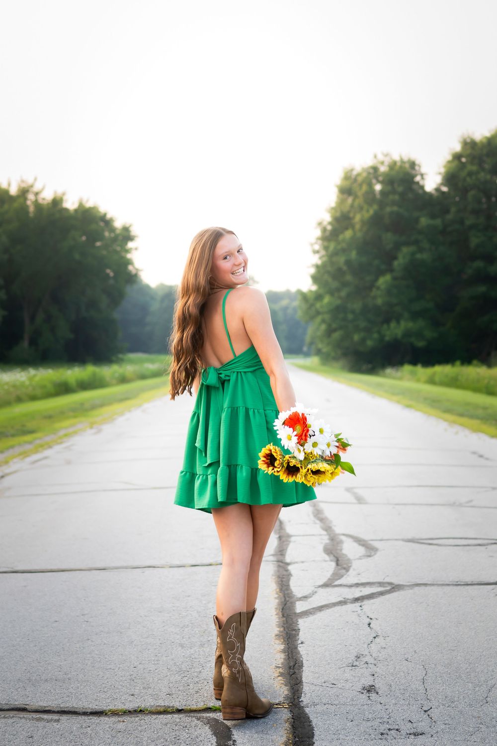 Green summer dress and cowboy boots make a statement on a rural concrete path.
