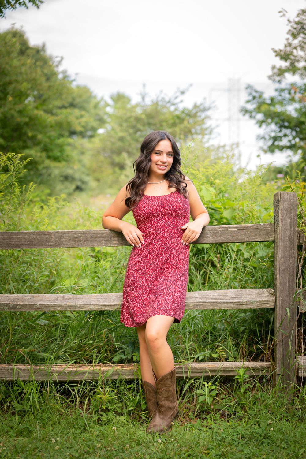 Red sundress and cowboy boots create a country charm look against a rustic wooden fence.