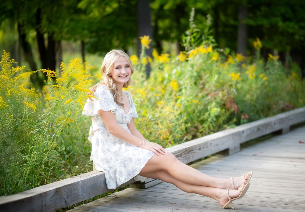 Summer portrait on a wooden walkway surrounded by lush yellow wildflowers and greenery.