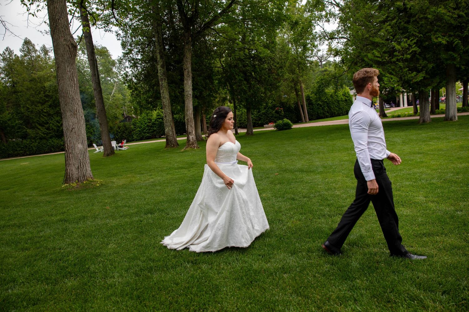 A couple in wedding attire walks through a lush green park on their special day as the sun disappears.