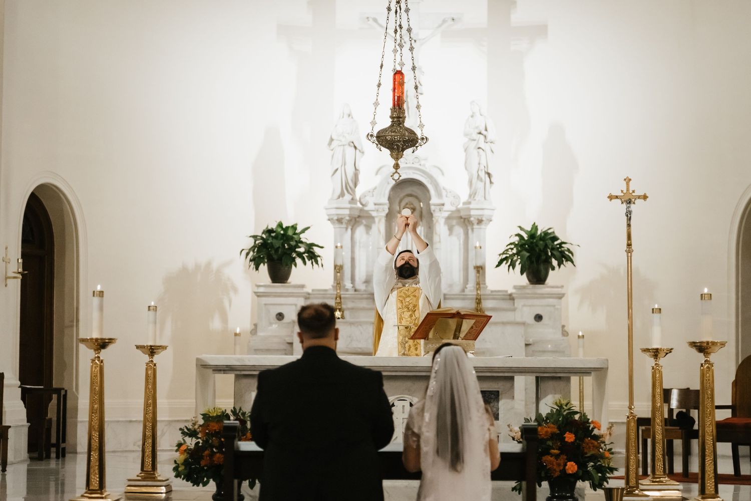 Interior view of a traditional white church sanctuary with altar, candles, and floral arrangements during a service.