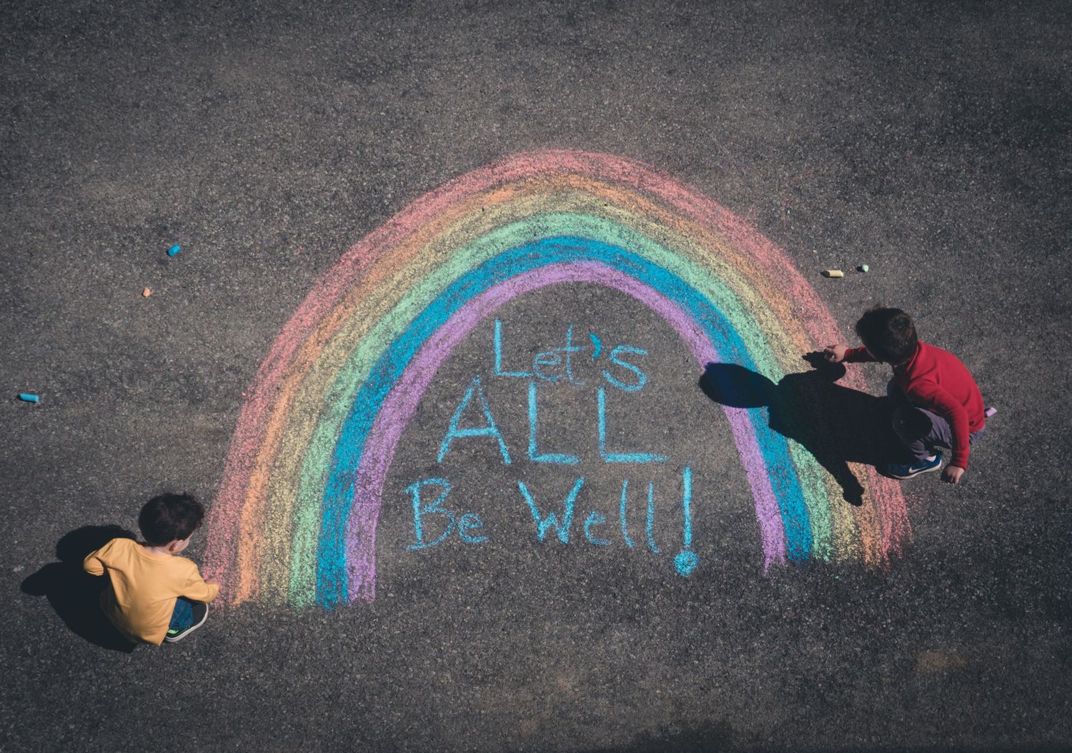 Sidewalk chalk rainbow drawings on dark pavement showing progression of artwork.
