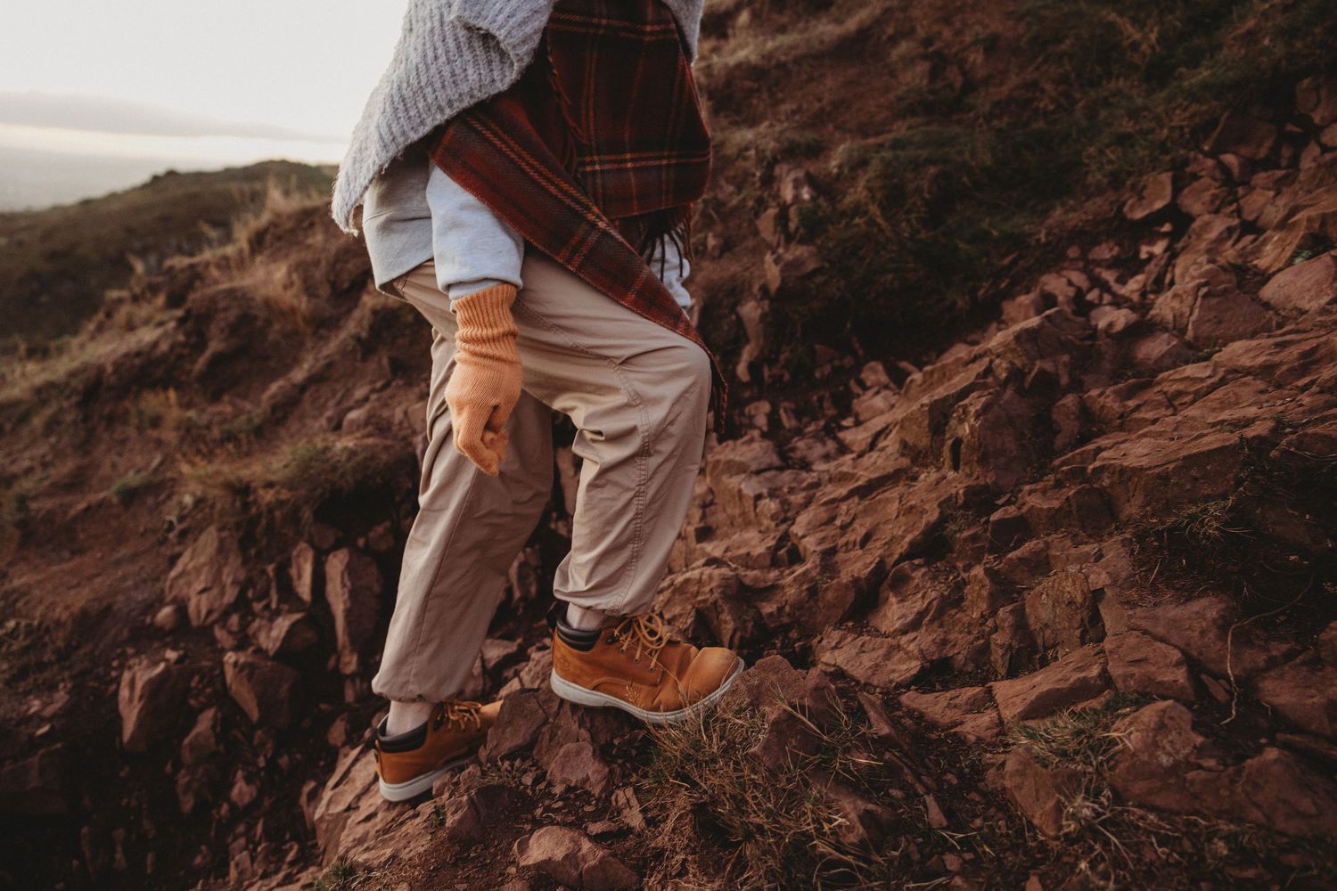 Hiker wearing brown boots and khaki pants stands on rugged red rock formations during outdoor adventure.