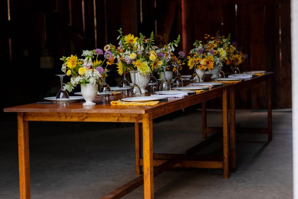 Rustic wooden tables decorated with white and yellow floral centerpieces line up in a dimly lit venue space.