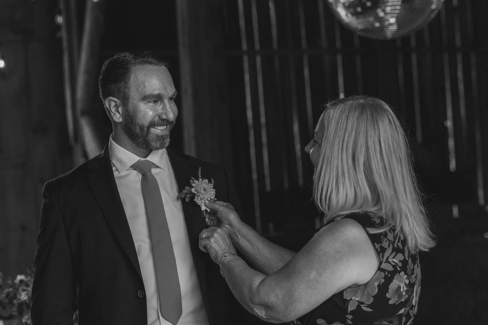 A black and white photo of a formal occasion showing a boutonniere being pinned onto a suit lapel.