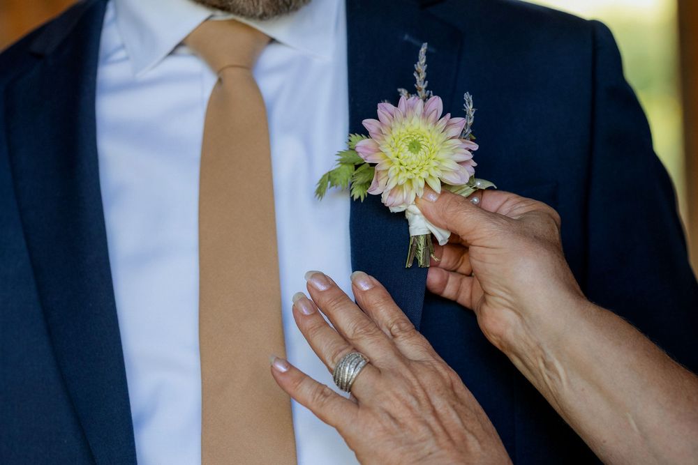A close-up sequence showing hands pinning a yellow chrysanthemum boutonniere to a navy suit lapel.
