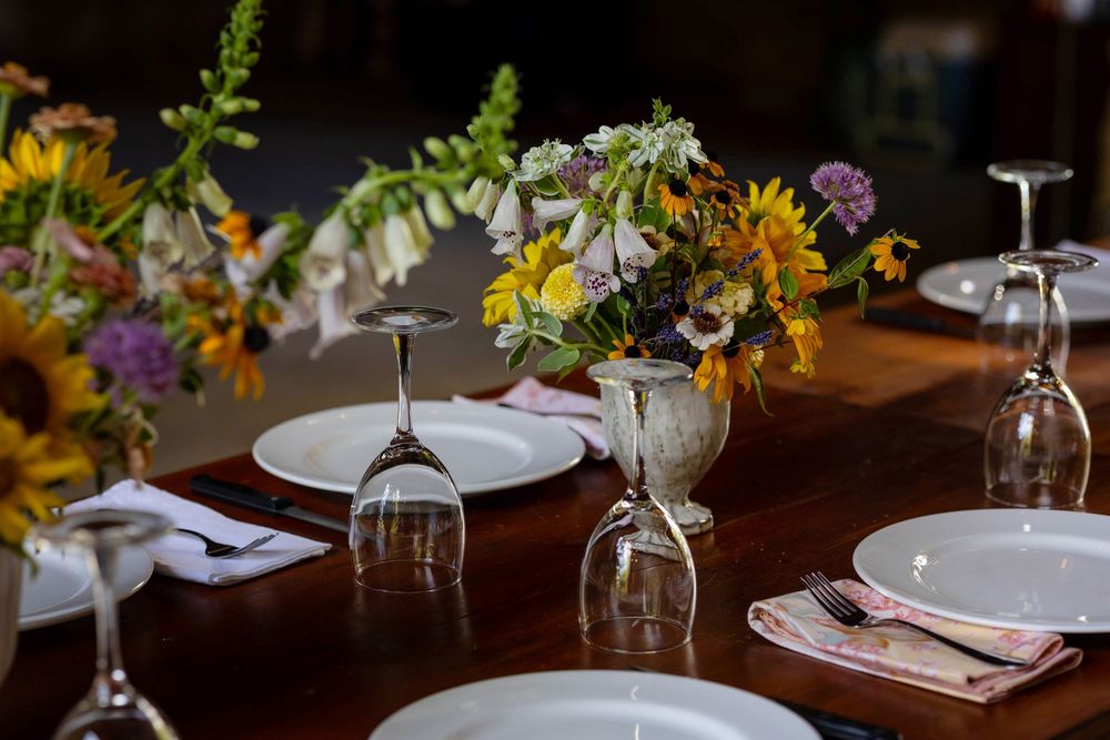 Elegant table setting with wine glasses and fresh floral arrangements at a rustic wooden dining table.