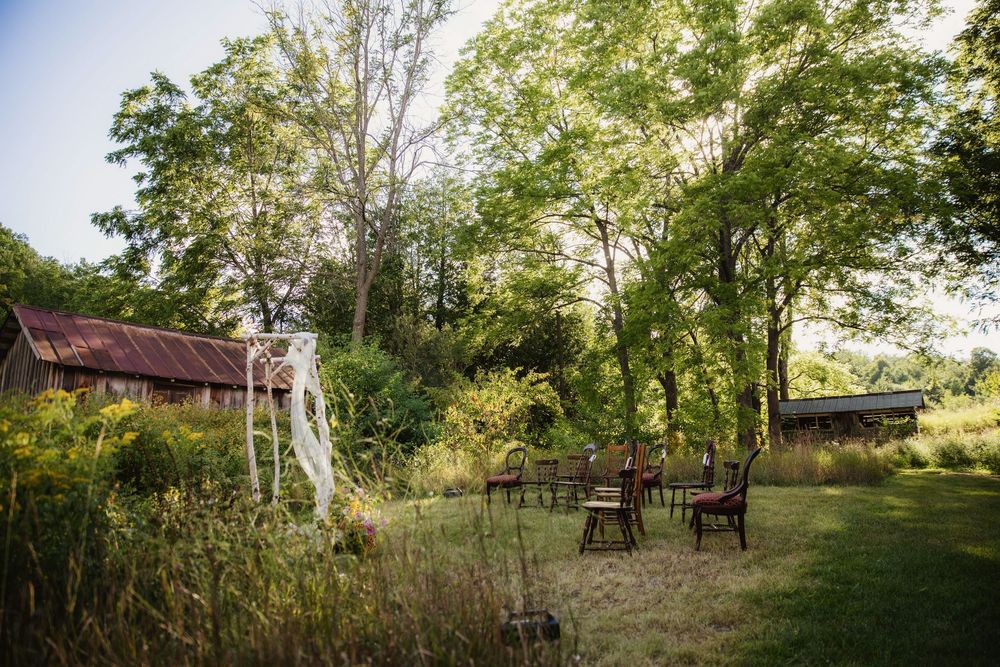 A serene garden path winds through lush green trees and landscaping with rustic outdoor furniture visible.