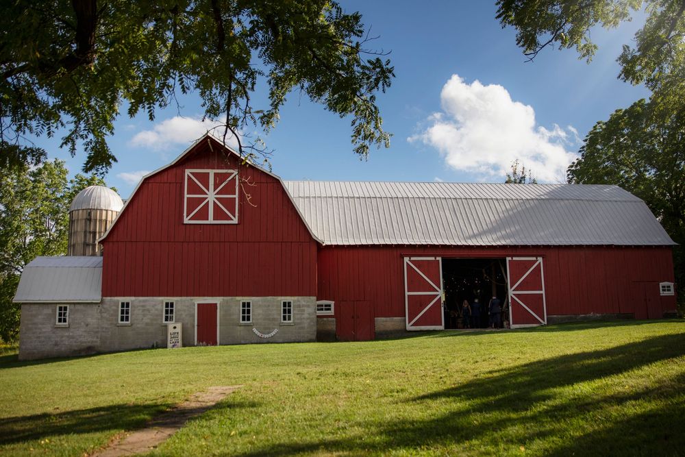 A panoramic view of traditional red barns and farm buildings set against a green hillside under a bright blue sky.