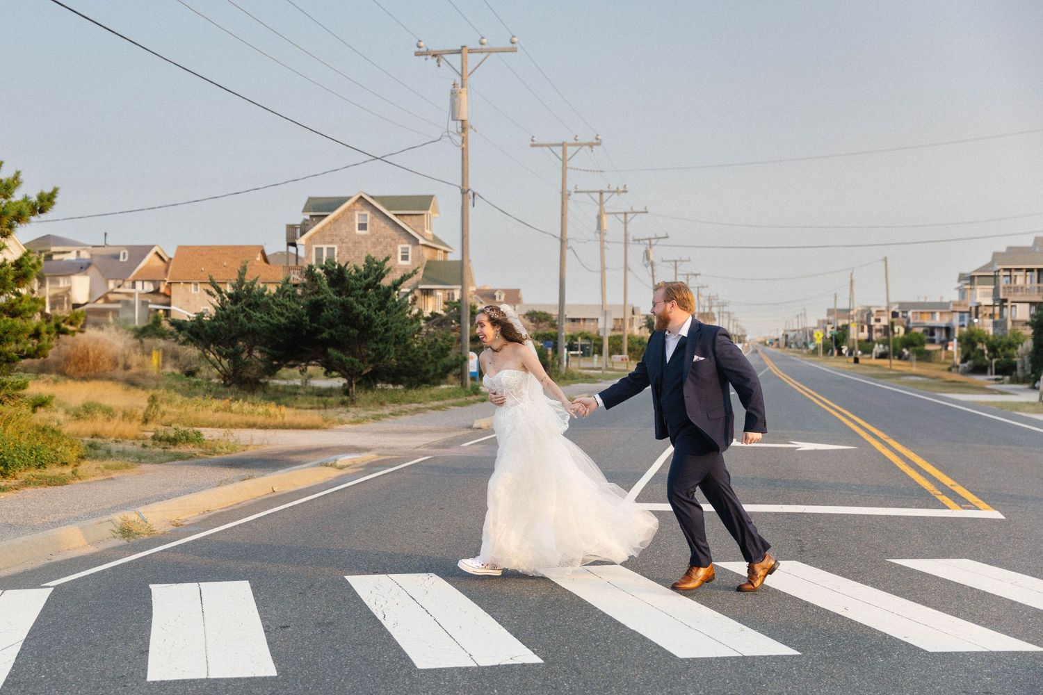 Couple in wedding attire playfully poses on crosswalk in suburban setting at sunset.