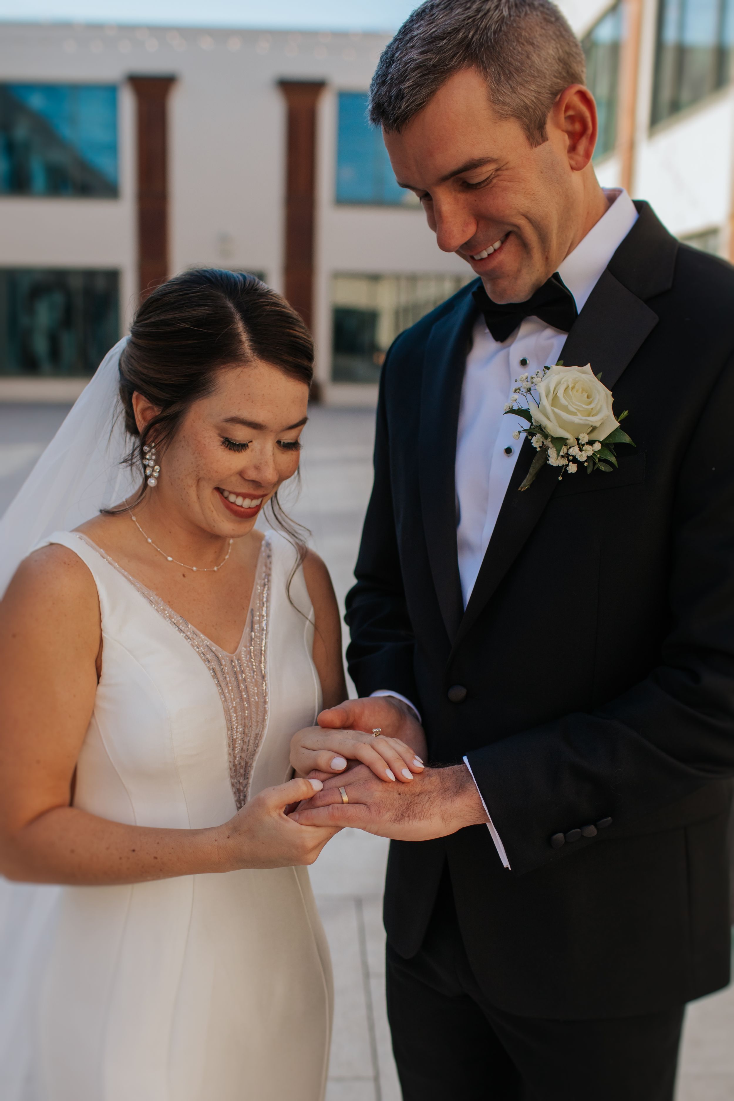 A joyful wedding moment as newlyweds share a laugh while looking at a ring during their outdoor ceremony.