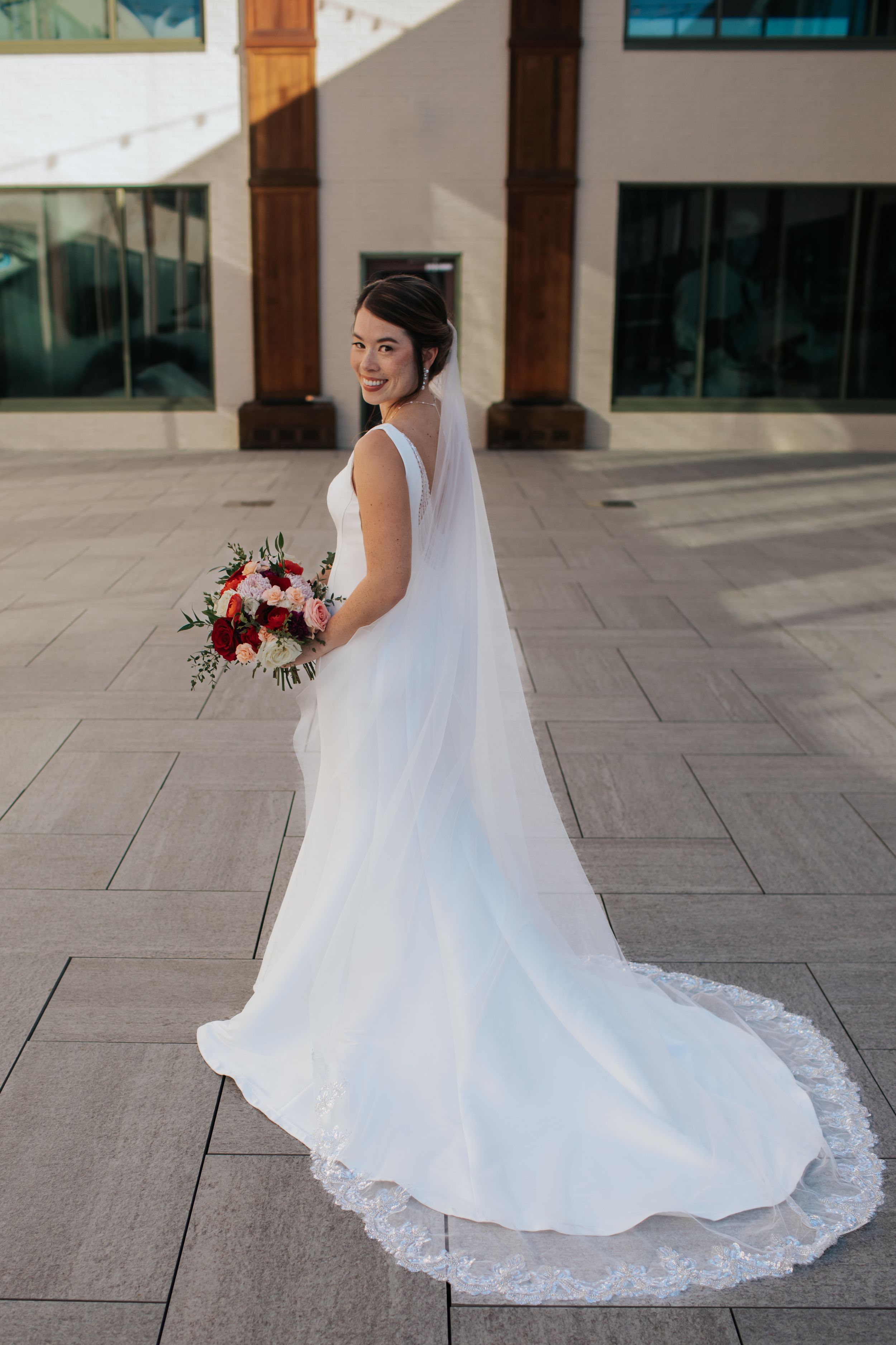 A bride in a flowing white wedding dress with lace trim twirls on a stone patio showing the elegant movement of her gown.