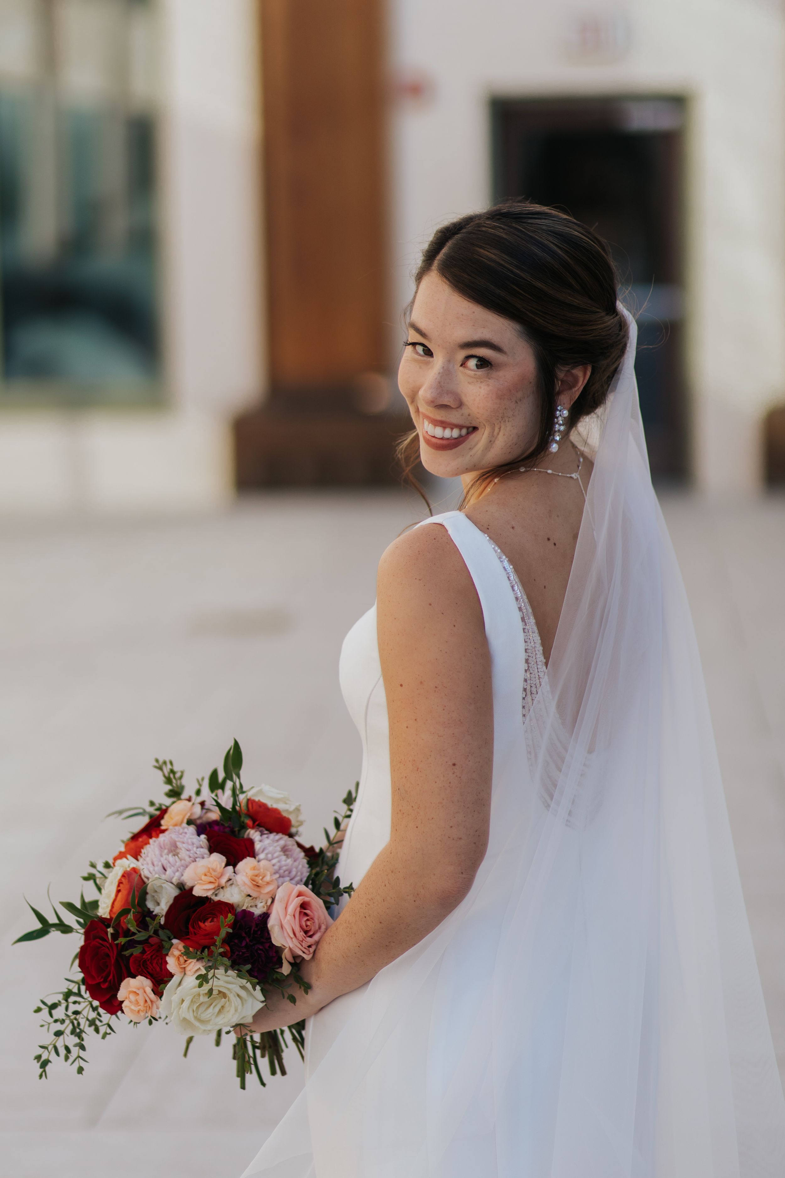 A bride in a white wedding dress holds a stunning burgundy and blush pink floral bouquet in a series of candid shots.