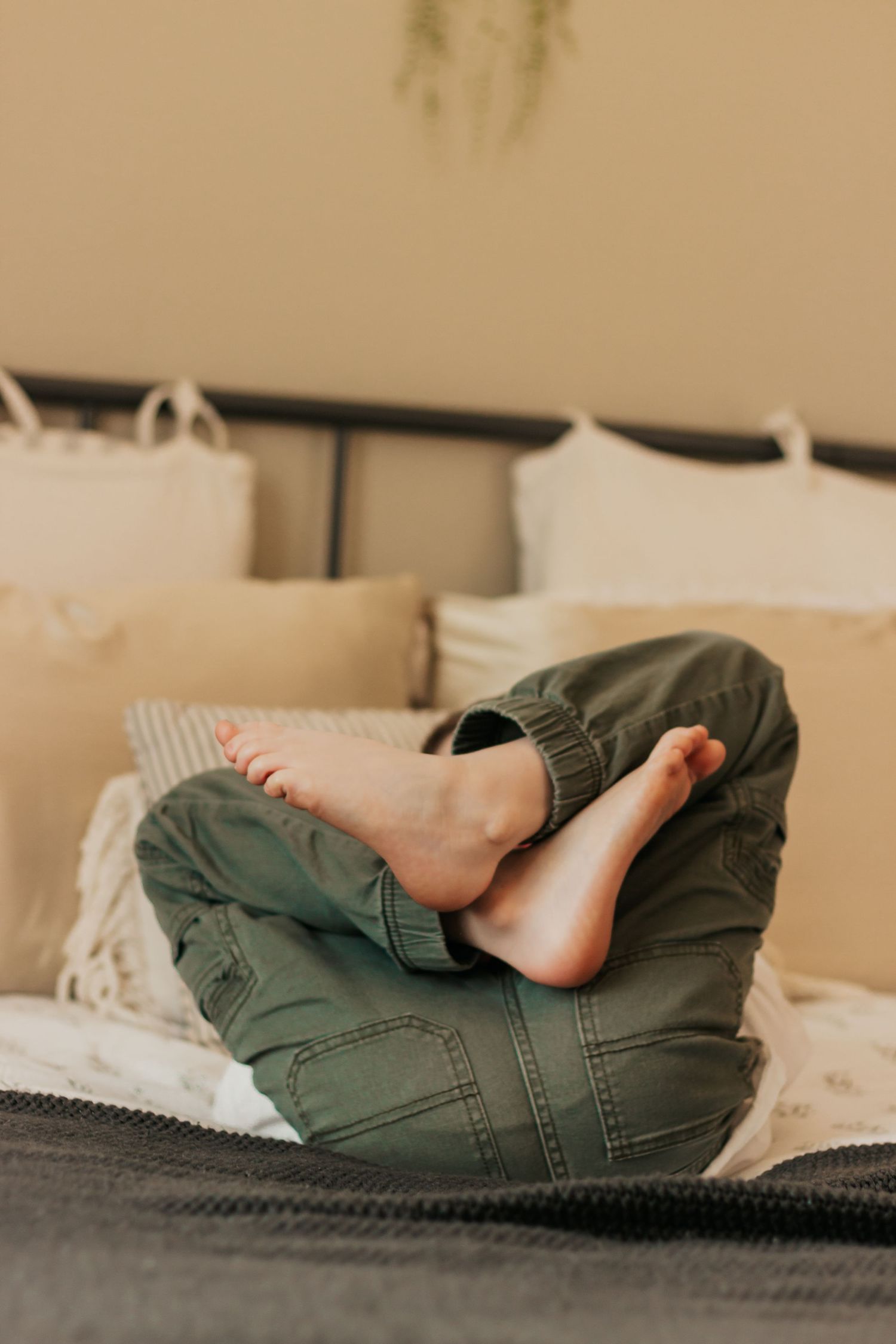 Bare feet peeking out from olive green pants while resting on a beige bedspread | Annual Birthday Photos for Kids