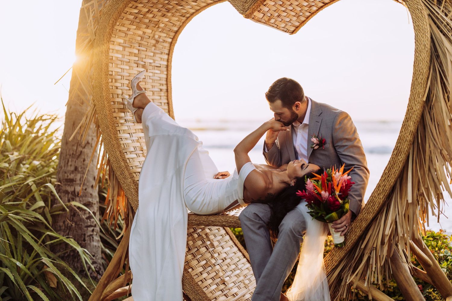 Romantic wedding scene under woven arch at sunset with tropical decor.