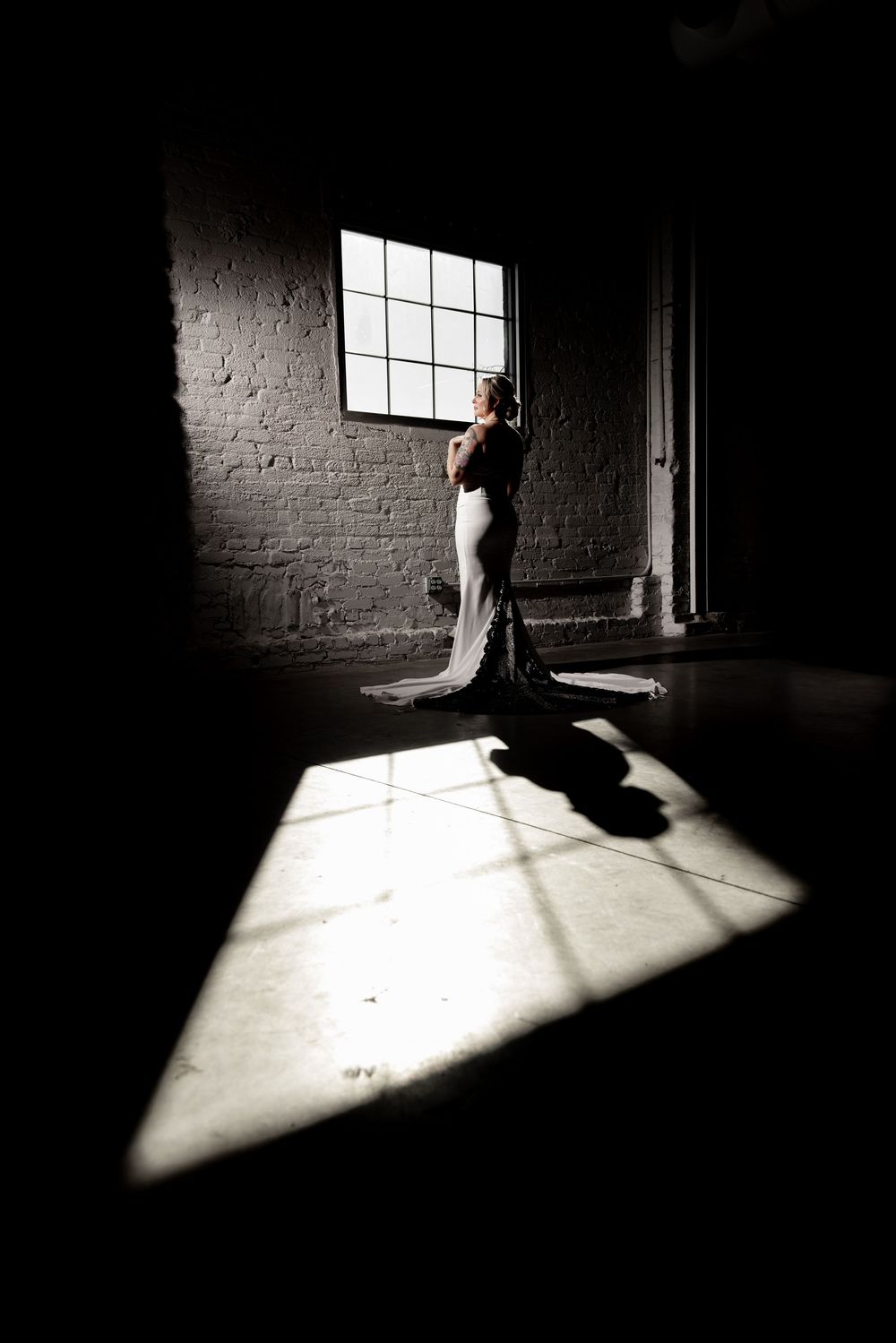 Silhouetted figure in an empty room with stark sunlight streaming through a window onto brick walls.