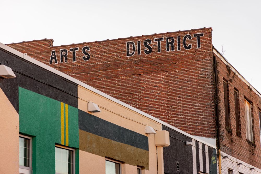 Exterior view of a brick building with Arts District signage and green awnings along a commercial street.