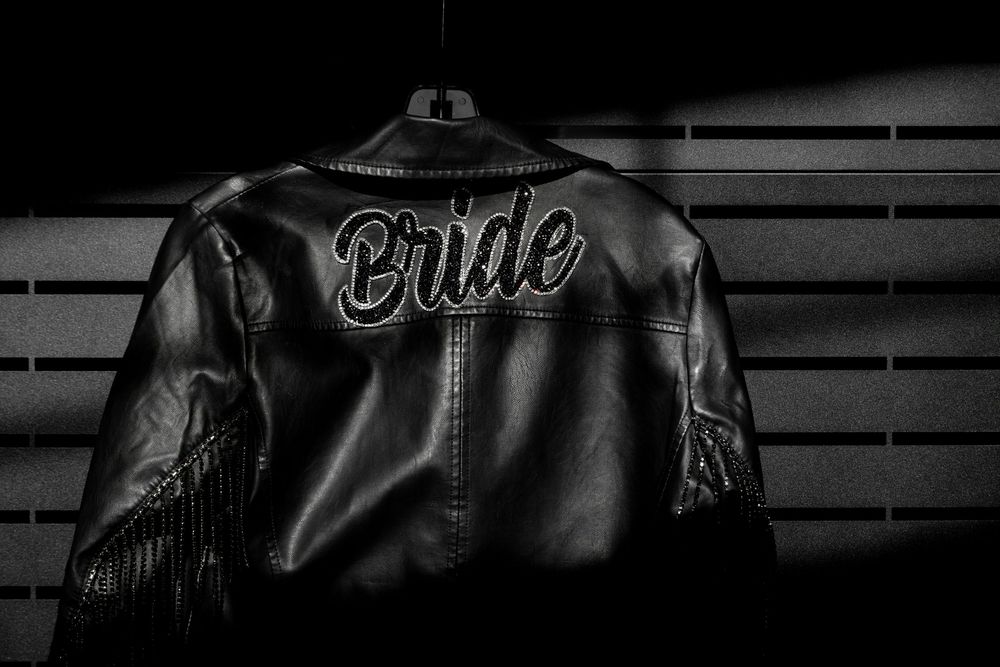 A dark leather jacket with embroidered text is displayed against a black background.