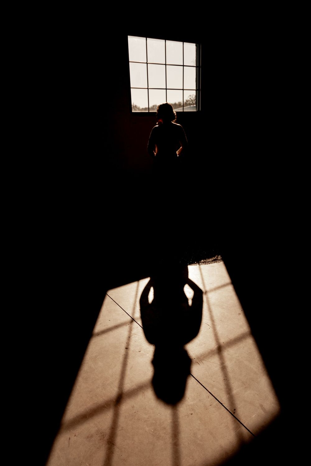 Dramatic shadows cast through a window onto a dark floor create geometric patterns in black and white.