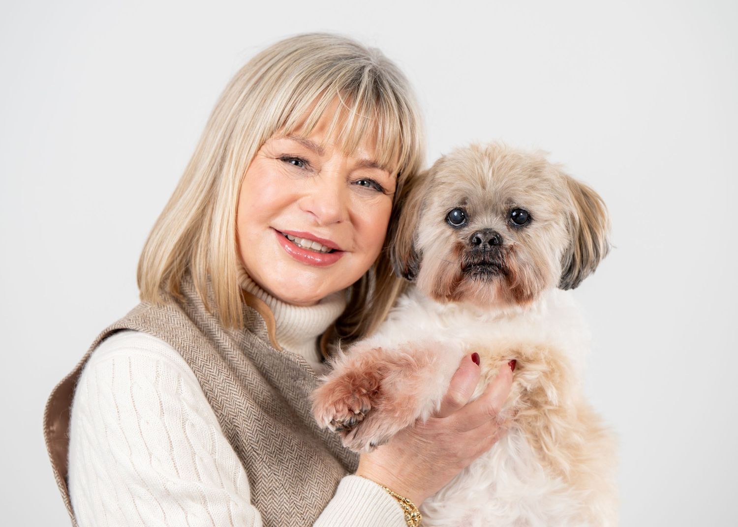 A small shaggy mixed breed dog with a scruffy beard being held against a white sweater.