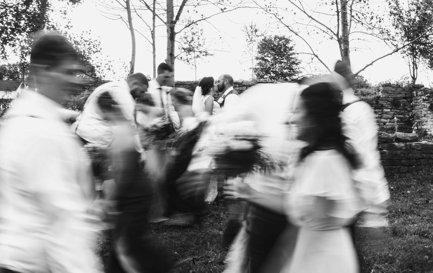 A motion-blurred black and white photograph of people dancing outdoors.
