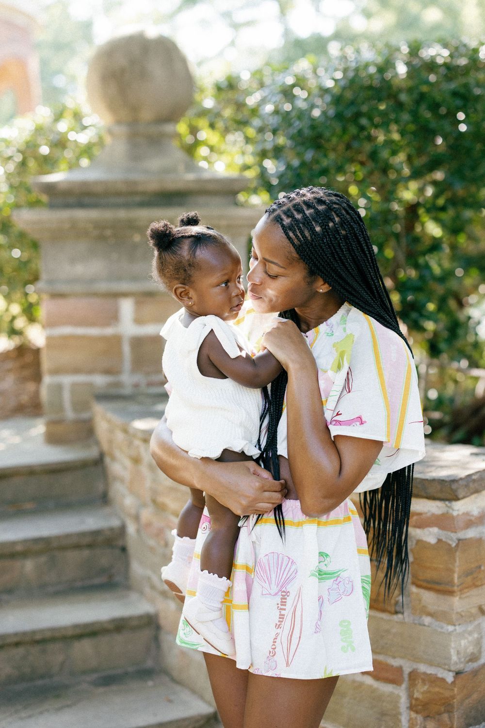 Four sequential photos showing a tender moment between a parent and child on stone steps in a sunny garden setting.