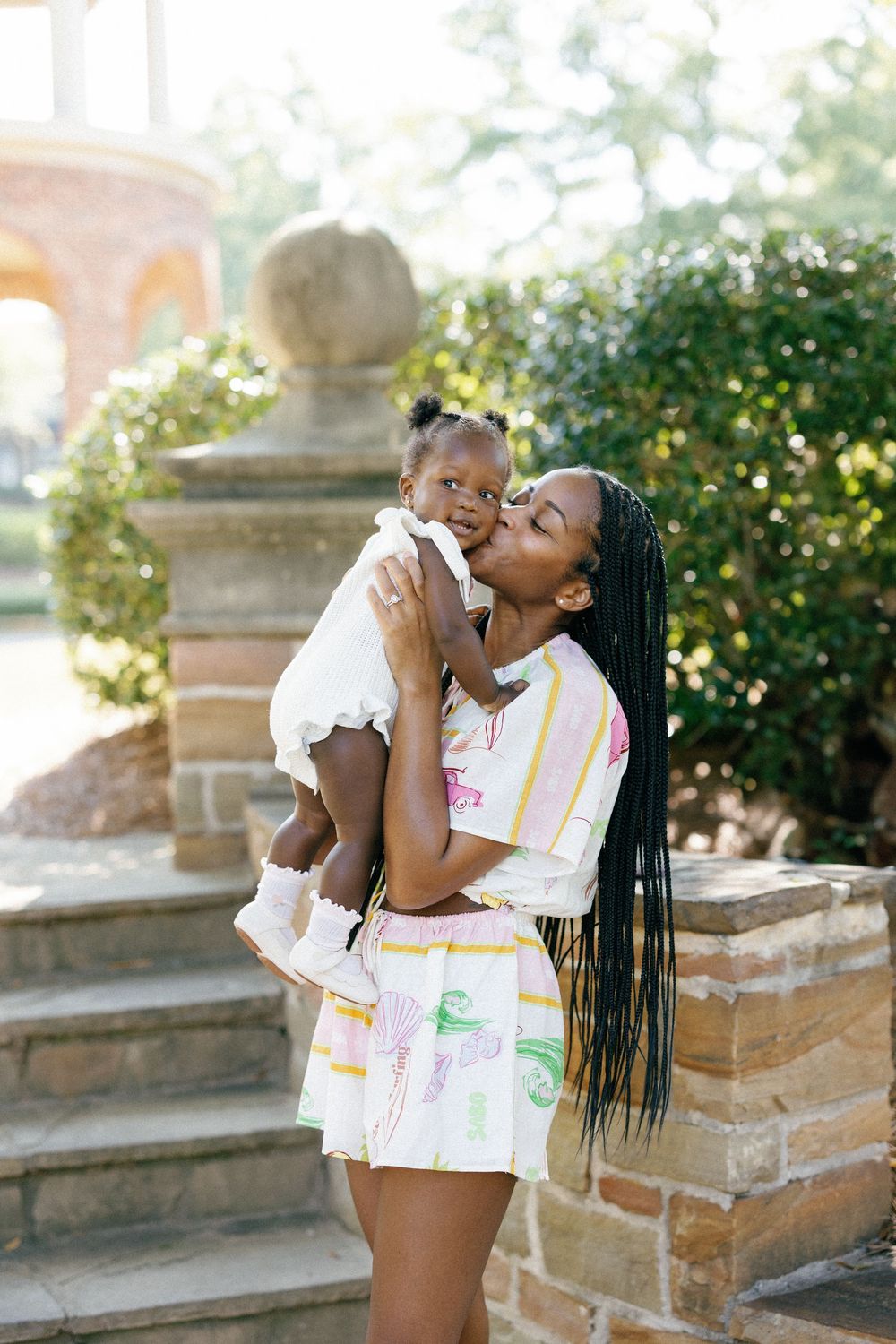 A person in a white outfit with braids laughs and dances joyfully against a stone wall background.