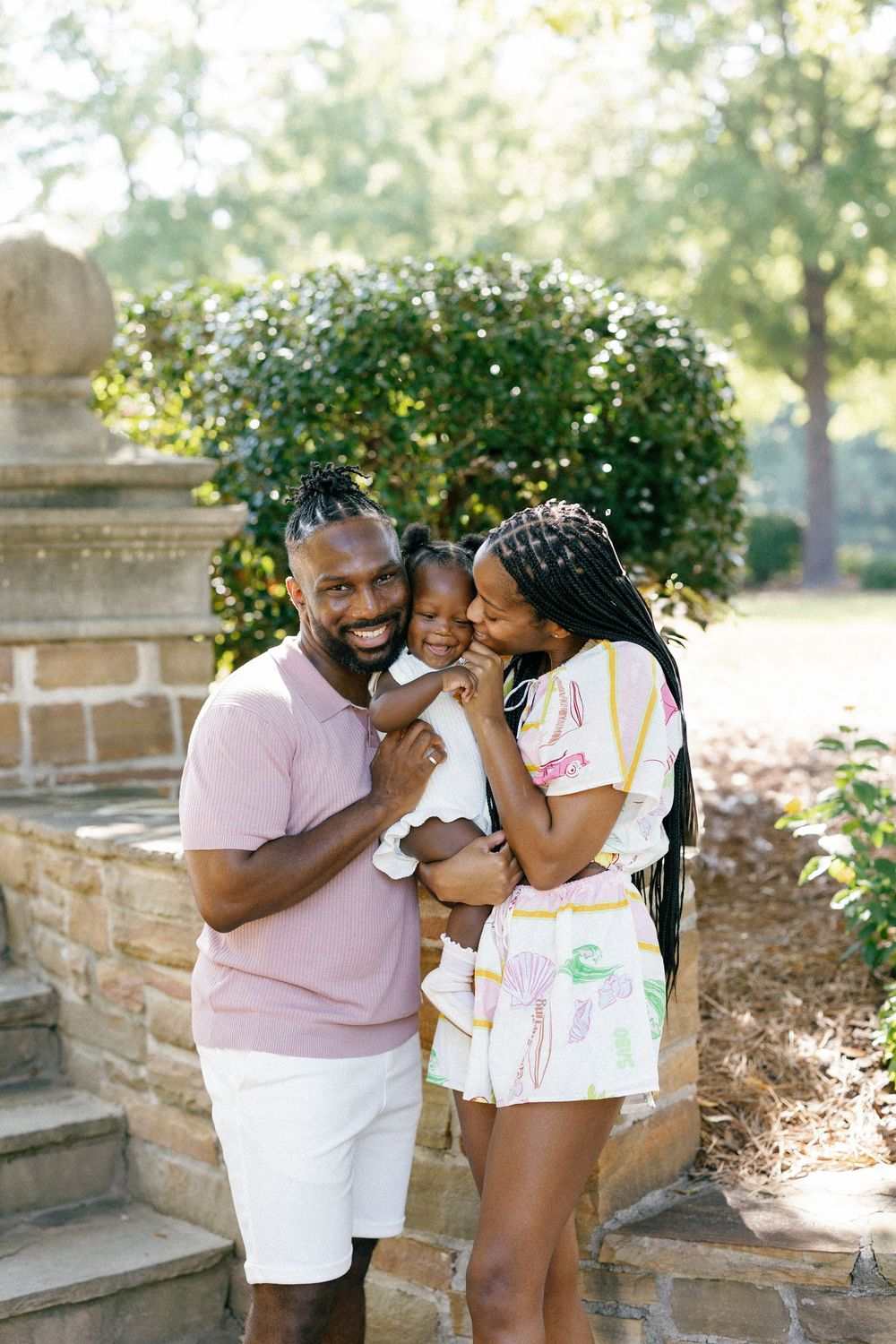 A joyful family shares a tender moment together on stone steps in a sunny garden setting.