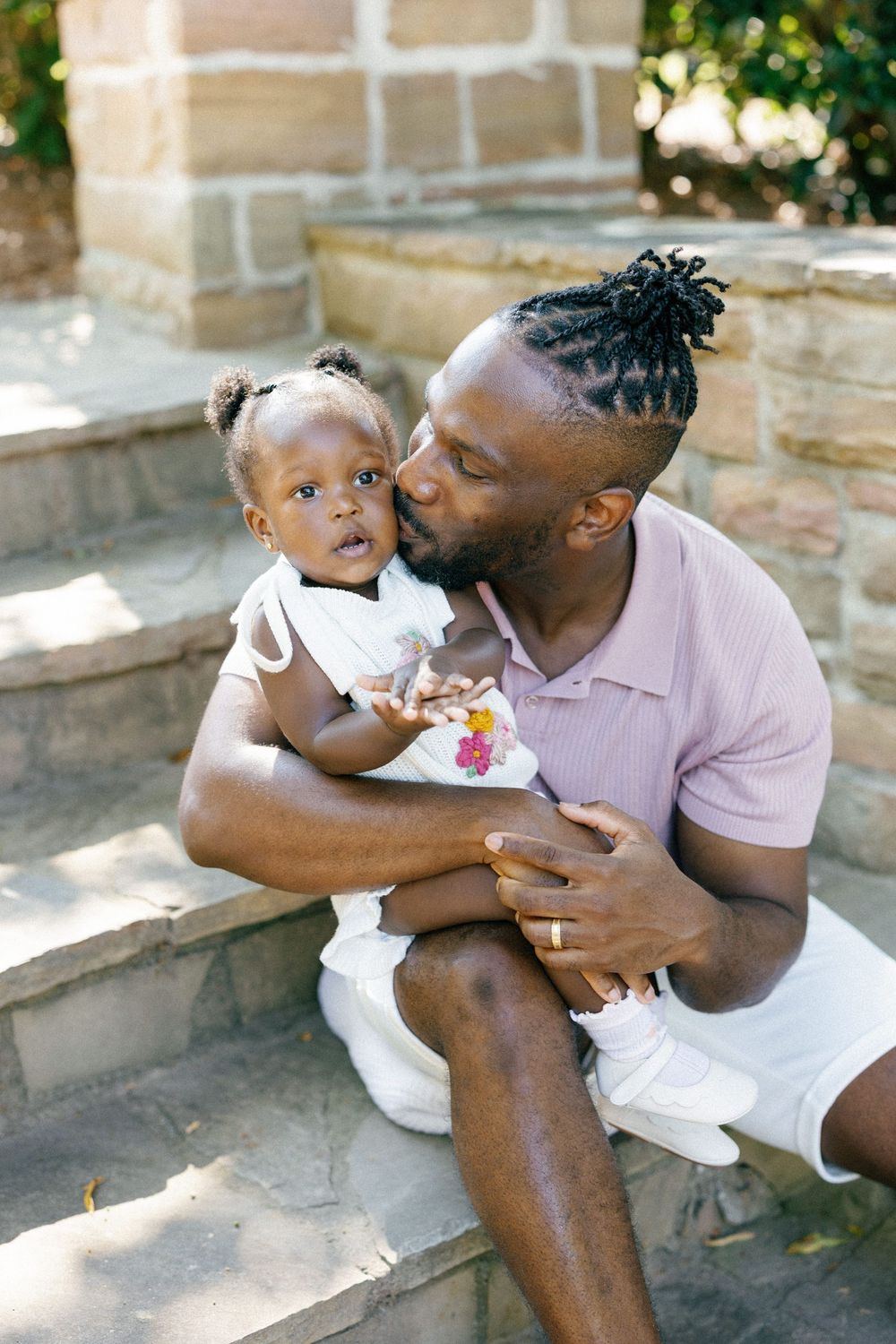 A tender moment shared between a parent and child sitting on stone steps outdoors on a sunny day.