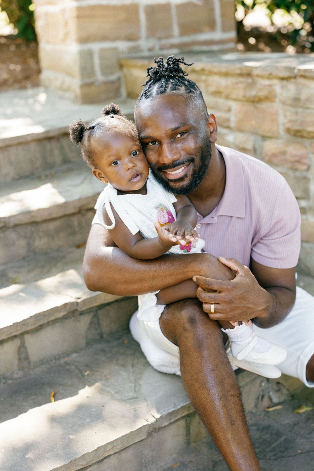 A parent and toddler share a joyful moment while sitting on stone steps in an outdoor setting.