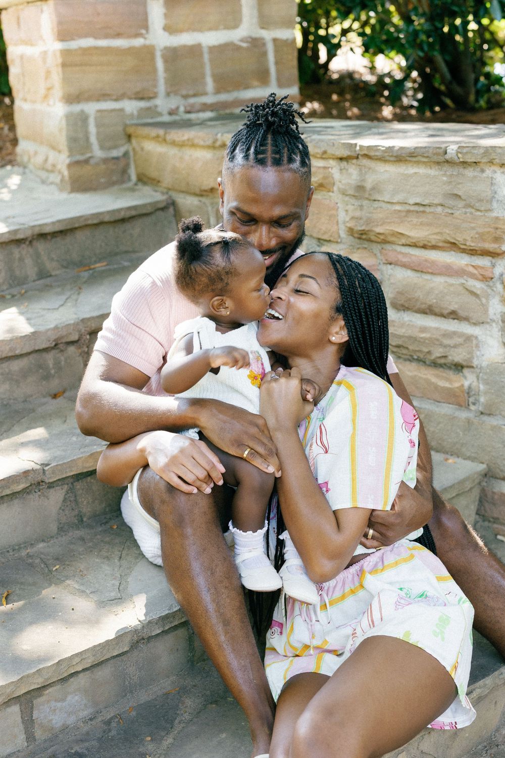 A loving family shares joyful moments together while sitting on stone steps outdoors on a sunny day.