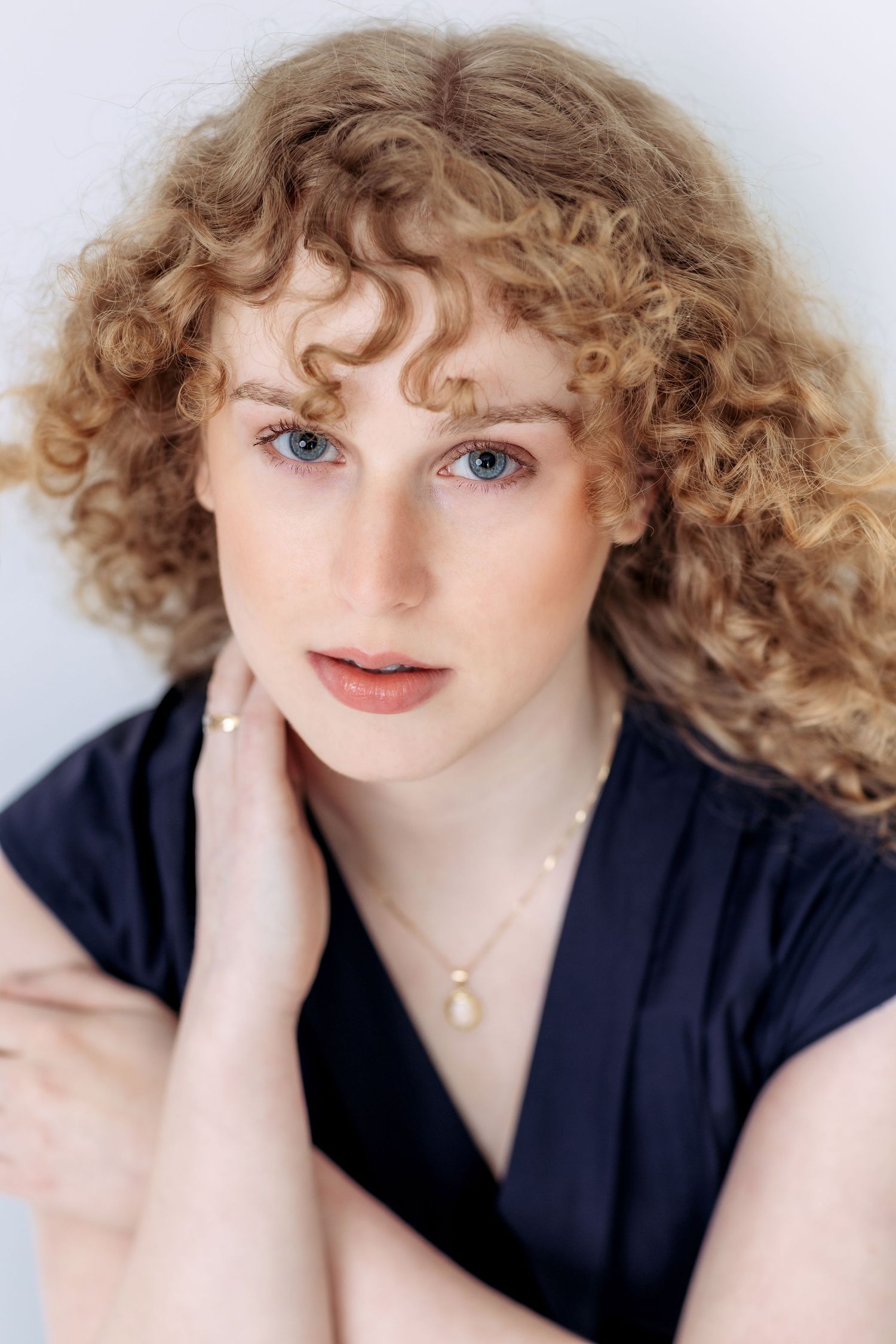 A series of five headshots showing curly blonde hair and blue eyes against a light background while wearing a navy top.