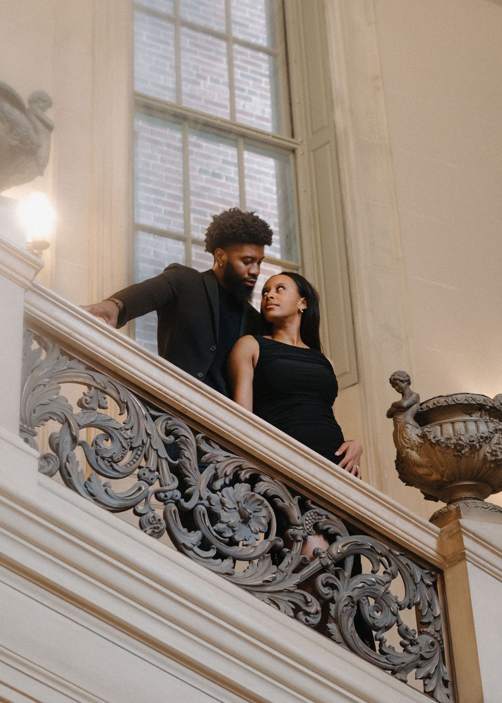 People pose on an elegant staircase with decorative iron railings and large windows.